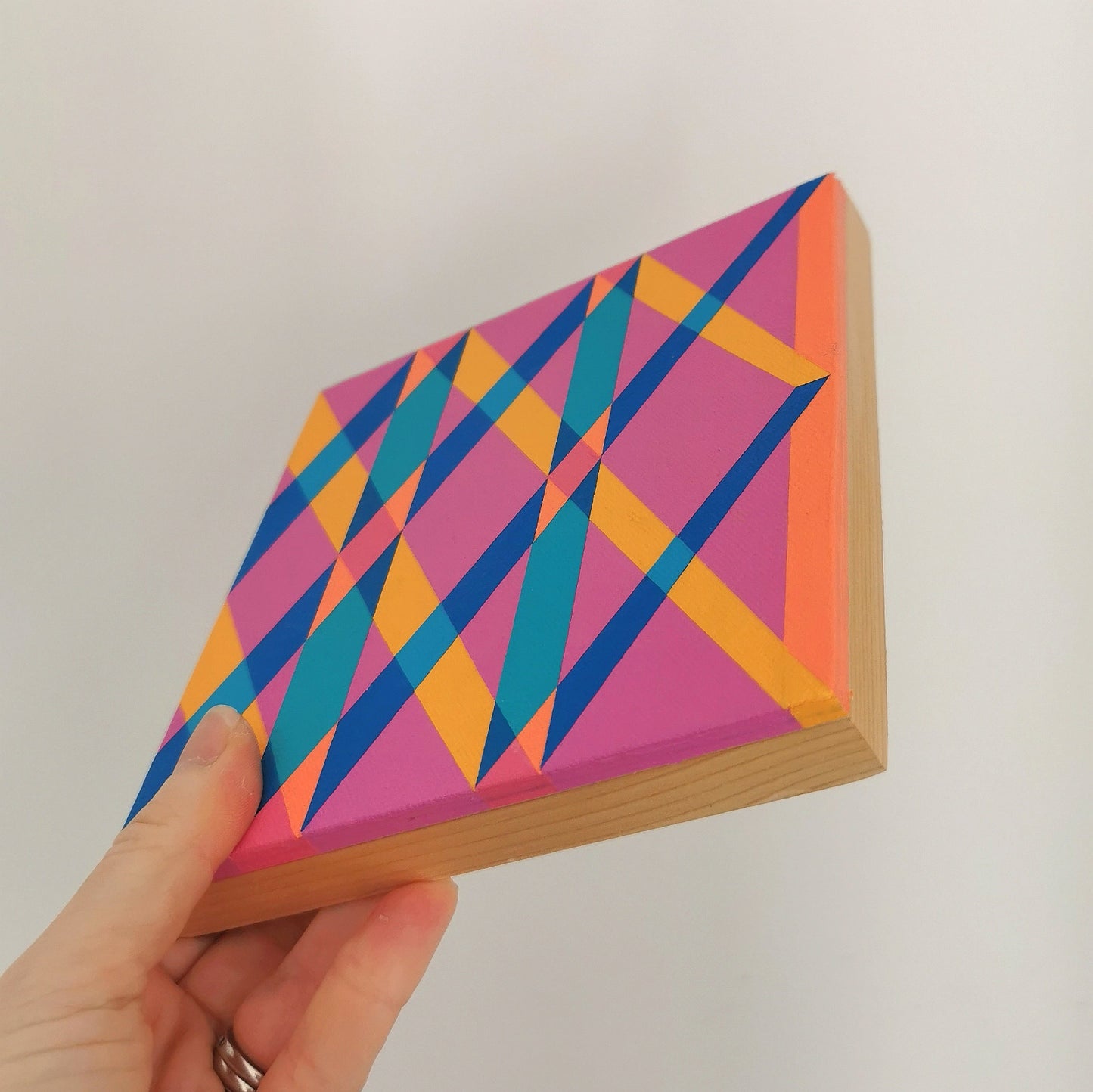 Hand holding “L PV19 PR122” – a small 15 x 15 cm canvas with a colourful geometric pattern. Part of Victoria Mardon’s B.E.L.O.N.G.I.N.G series, shown for scale.
