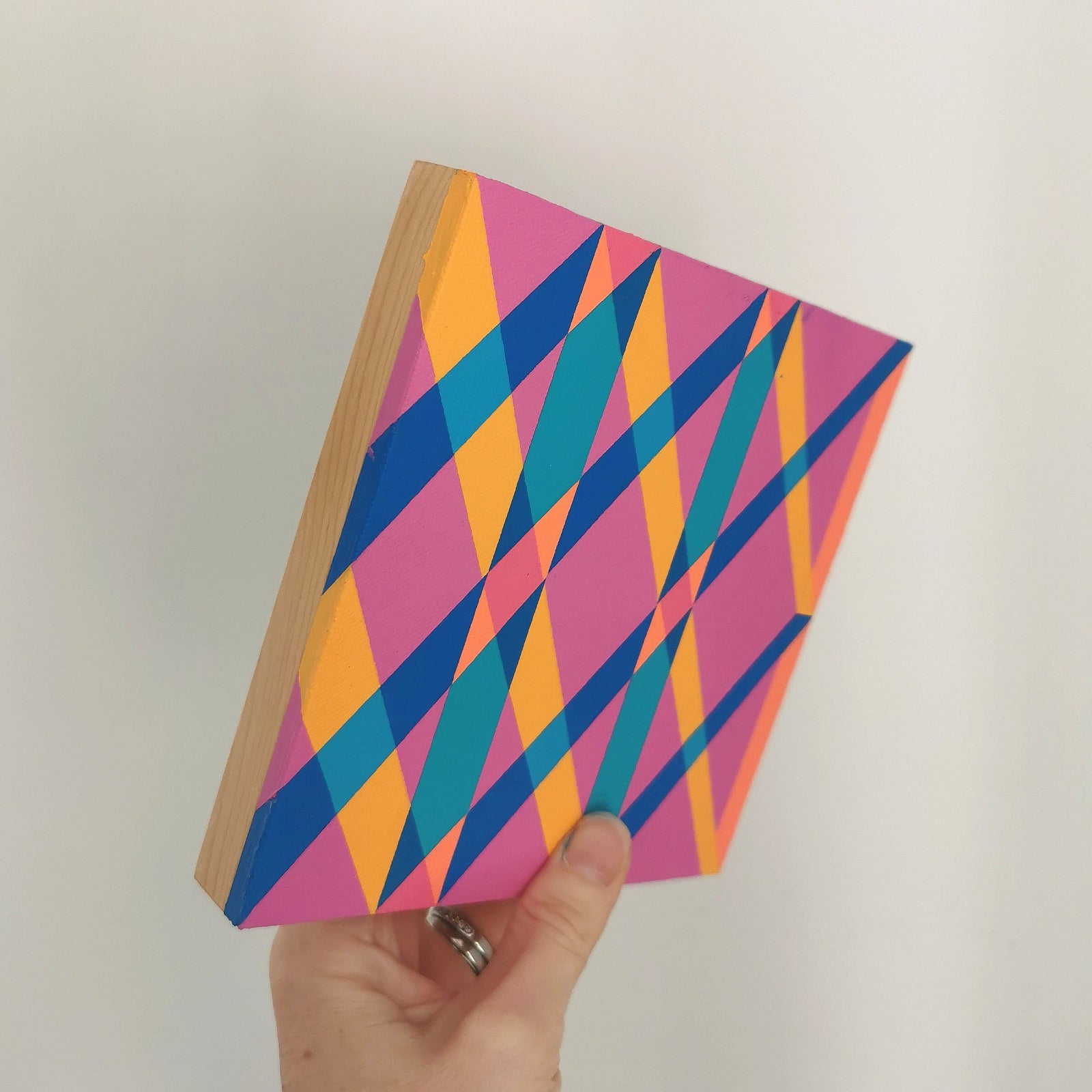 Hand holding “G2 PV19 PR122” – a small 15 x 15 cm canvas with a colourful geometric pattern. Part of Victoria Mardon’s B.E.L.O.N.G.I.N.G series, shown for scale.