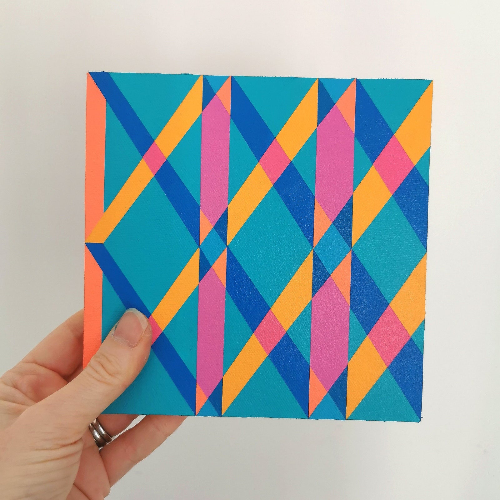 Hand holding “I PG7/PB15:3 – PB15:3/PG7” – a small 15 x 15 cm canvas with a colourful geometric pattern. Part of Victoria Mardon’s B.E.L.O.N.G.I.N.G series, shown for scale.
