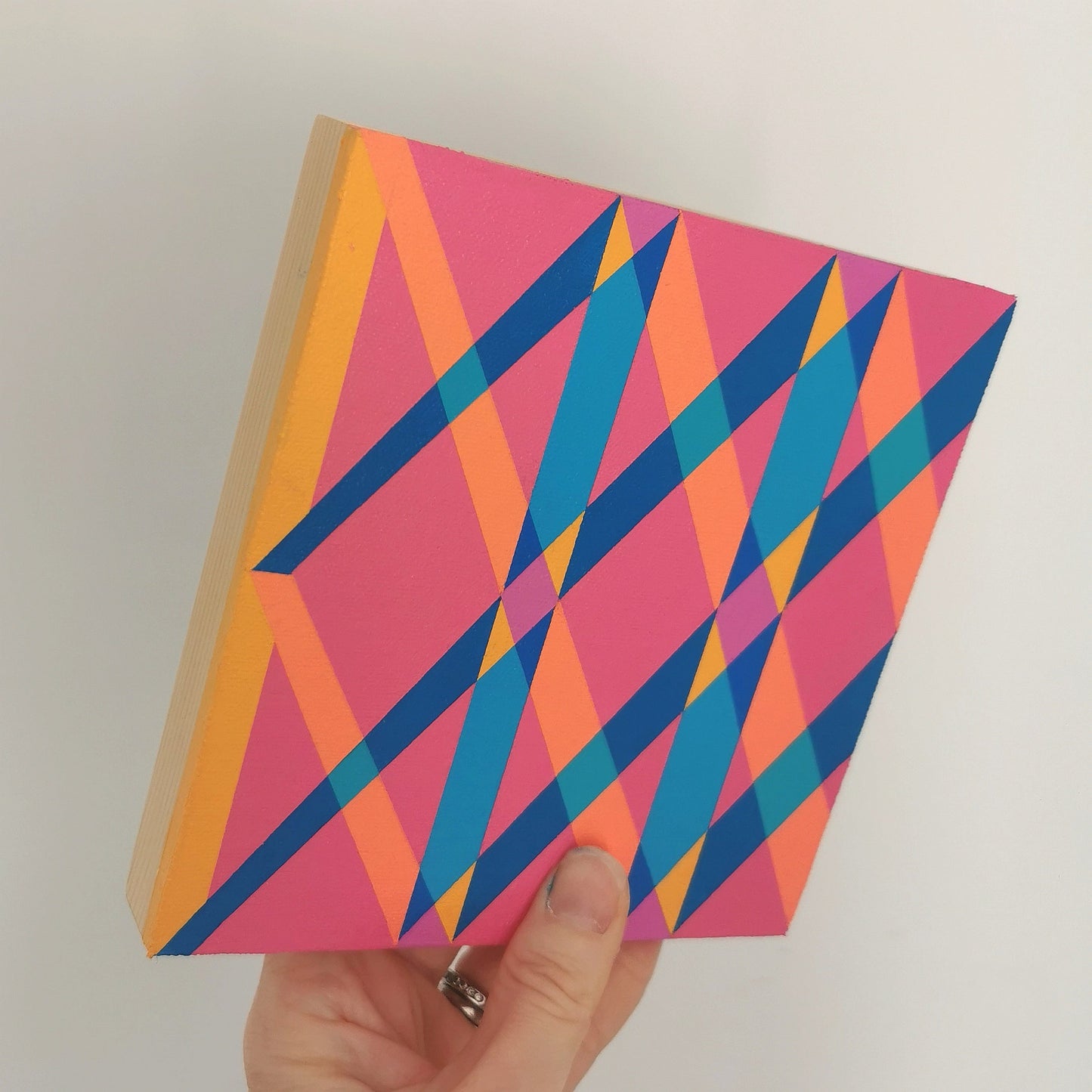 Hand holding “I PV19 PR122” – a small 15 x 15 cm canvas with a colourful geometric pattern. Part of Victoria Mardon’s B.E.L.O.N.G.I.N.G series, shown for scale.
