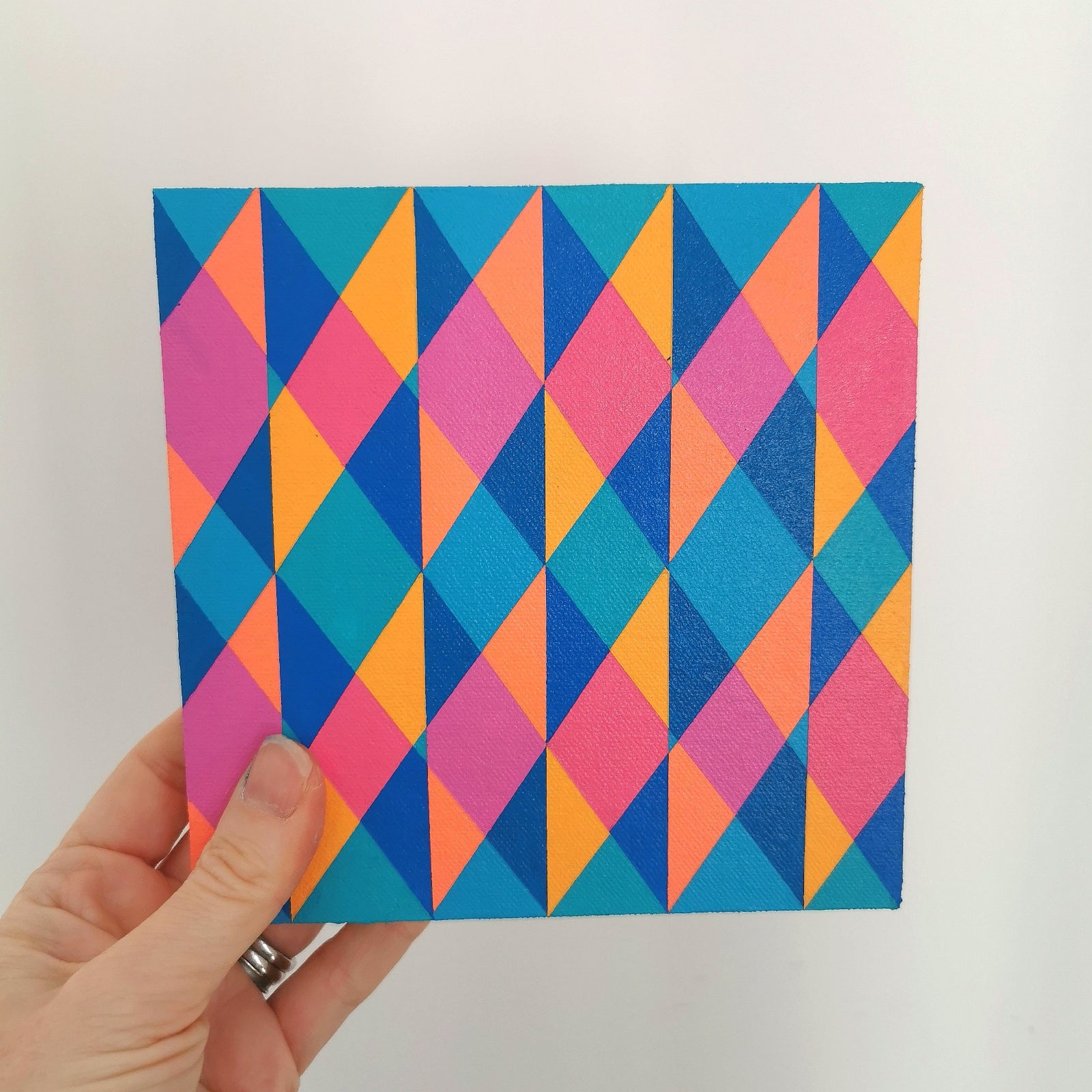 Hand holding “N2 PG7/PB15:3 – PB15:3/PG7” – a small 15 x 15 cm canvas with a colourful geometric pattern. Part of Victoria Mardon’s B.E.L.O.N.G.I.N.G series, shown for scale.