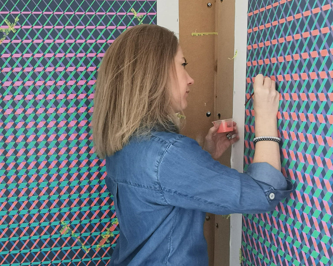 Side view of artist Victoria Mardon painting a complex geometric abstract in her studio. Captures the creative process and vibrant work in progress.