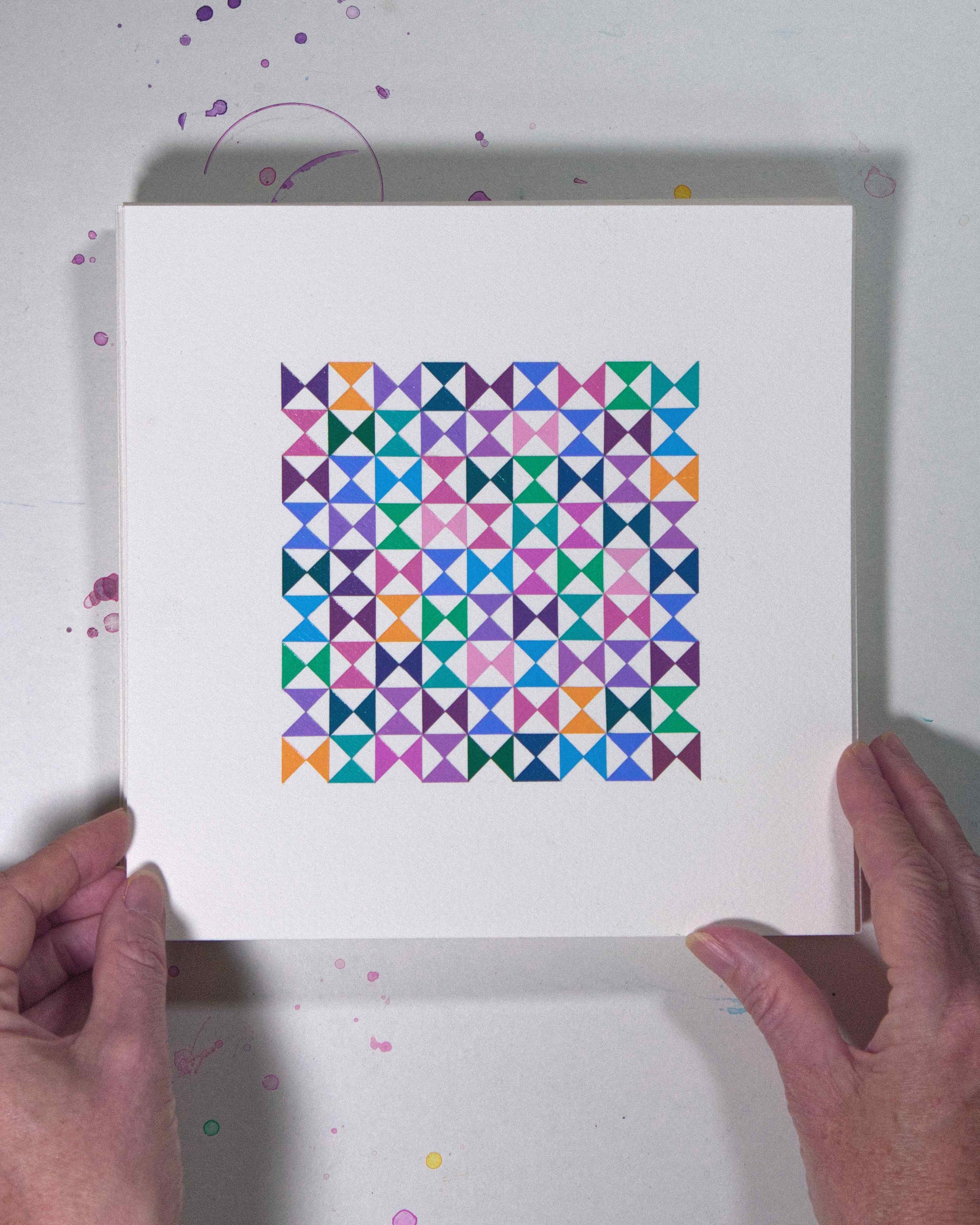 Hands holding a bold, graphic multicoloured abstract painting with repeating geometric shapes, 1 July – 001/365 (46204/365) by Victoria Mardon, 365: A Year in Colour series.